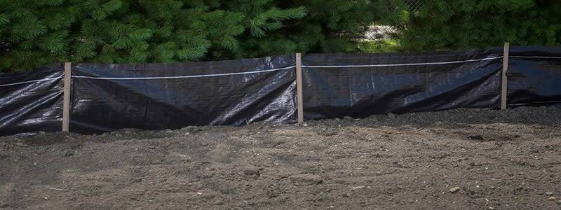 Silt fence fabrics are assembled with wood stakes and set on the soil.